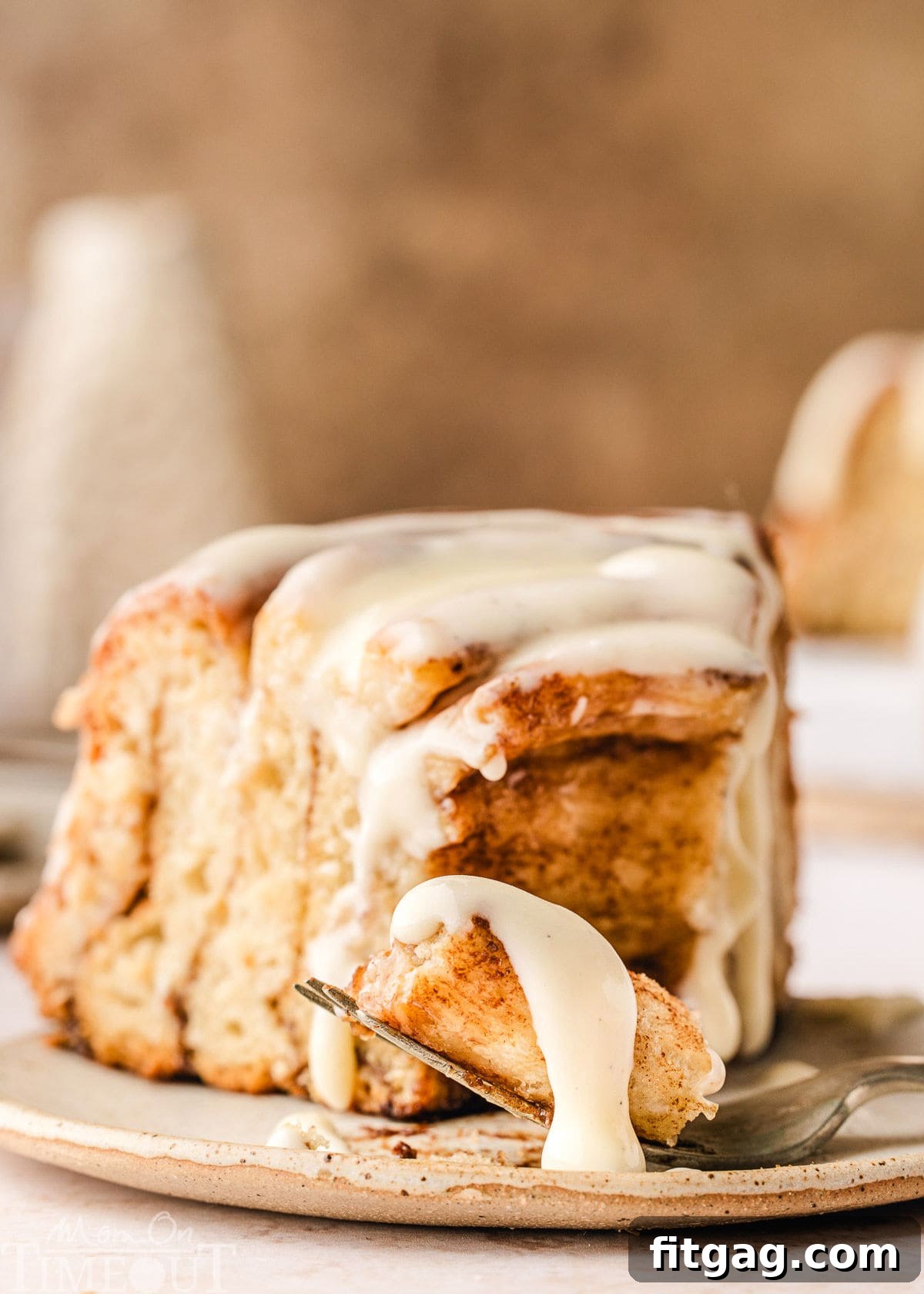 Colossal Cinnamon Swirl Cake 3 Slice of giant cinnamon roll cake recipe on small white plate. Cake has been drizzled with cream cheese glaze. A fork has taken the tip off the slice.