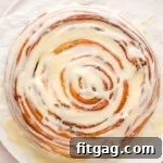 Colossal Cinnamon Swirl Cake 10 top down view of a giant cinnamon roll cake sitting on a white piece of parchment paper with a cream cheese glaze generously drizzled over the top.