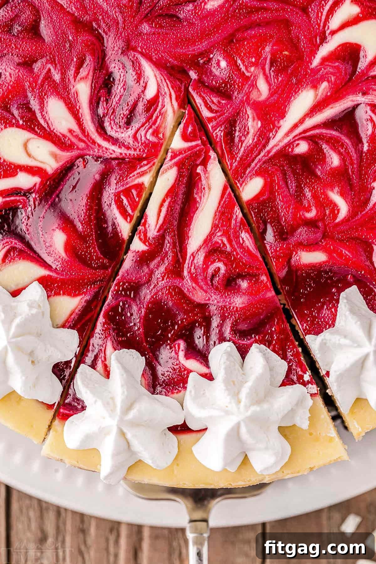 Velvet White Chocolate Raspberry Bliss 4 A top-down shot showing a slice of white chocolate raspberry cheesecake being carefully lifted from the whole cake, revealing its perfectly set texture and the delicious layers.