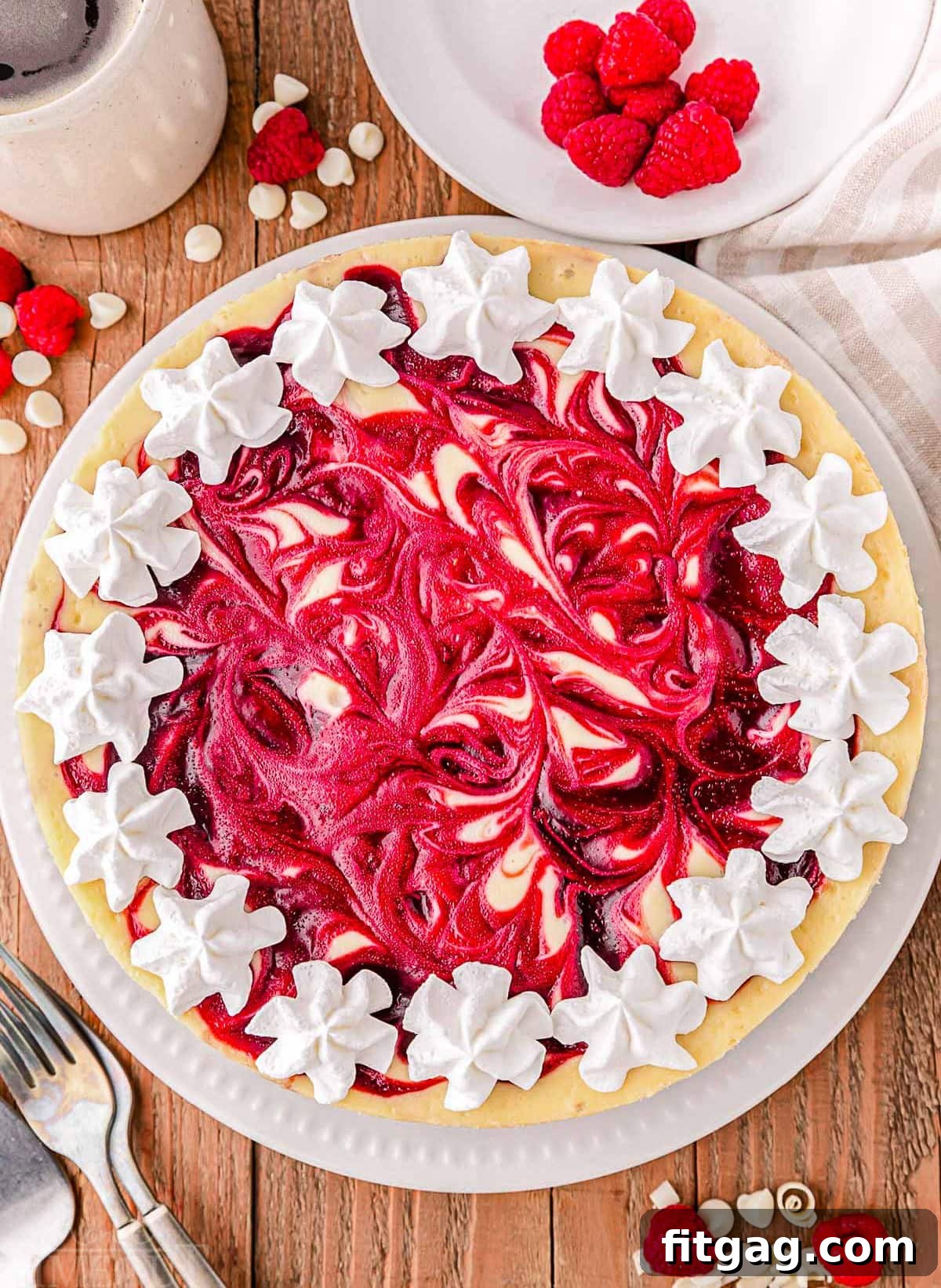 Velvet White Chocolate Raspberry Bliss 5 A mesmerizing top-down view of the entire White Chocolate Raspberry Cheesecake, beautifully adorned with a luscious raspberry swirl and artfully garnished with delicate dollops of fresh whipped cream and ripe raspberries.