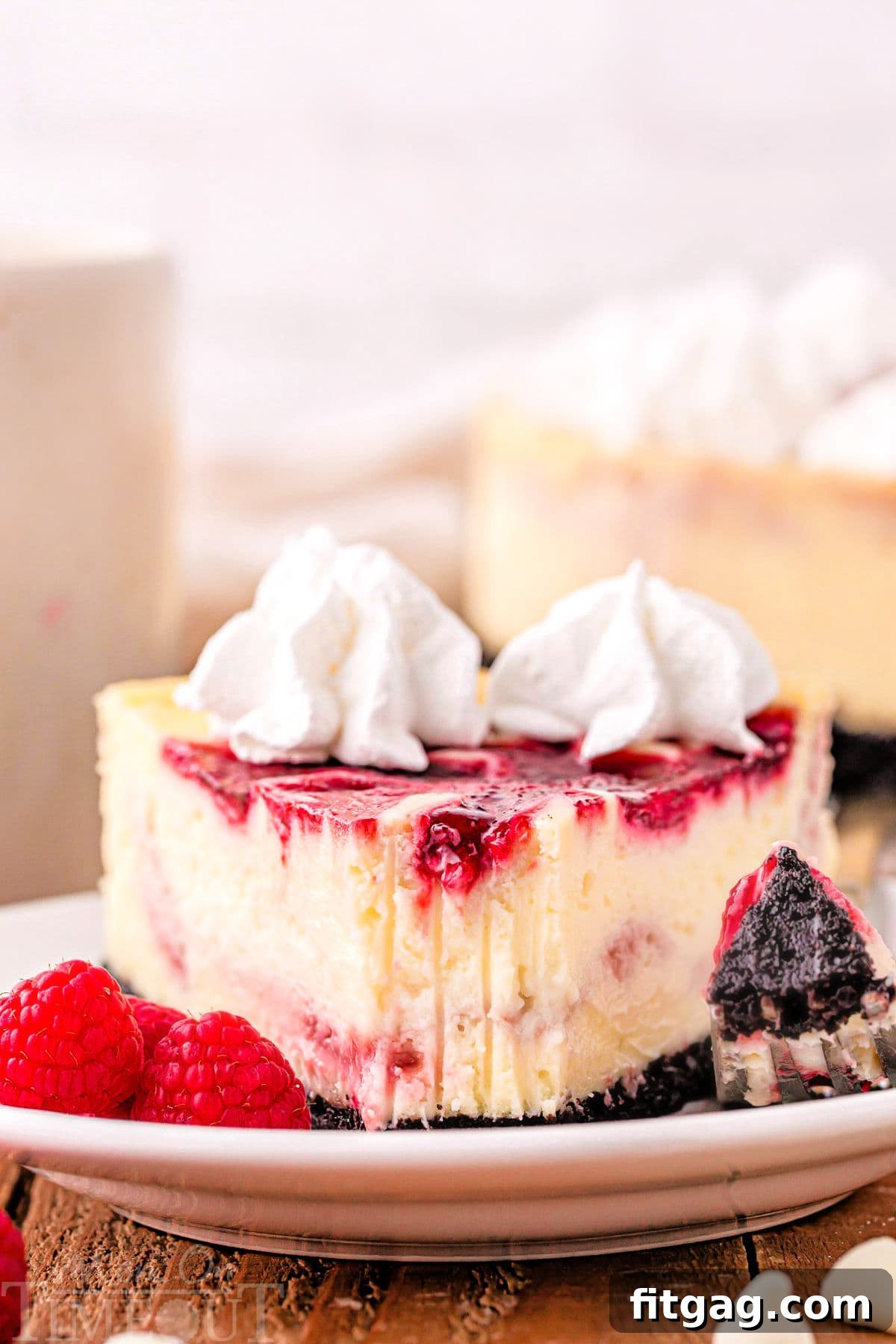 Velvet White Chocolate Raspberry Bliss 6 A close-up shot of a perfect piece of White Chocolate Raspberry Cheesecake with one bite removed, revealing the creamy texture and the impress of a fork tines.
