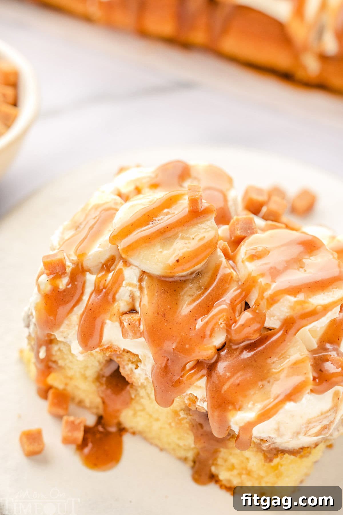 An inviting top-down, angled view of a single slice of Banoffee Poke Cake resting on a round white plate, beautifully showing off its layers and toppings.