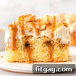 piece of banoffee poke cake on a white plate. the cake has been topped with whipped cream, bananas and dulce de leche sauce.