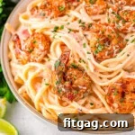 Close up look at bowl of cajun shrimp pasta recipe with a rich Parmesan cream sauce and topped with spicy shrimp and garnished with fresh parsley and Parmesan cheese.