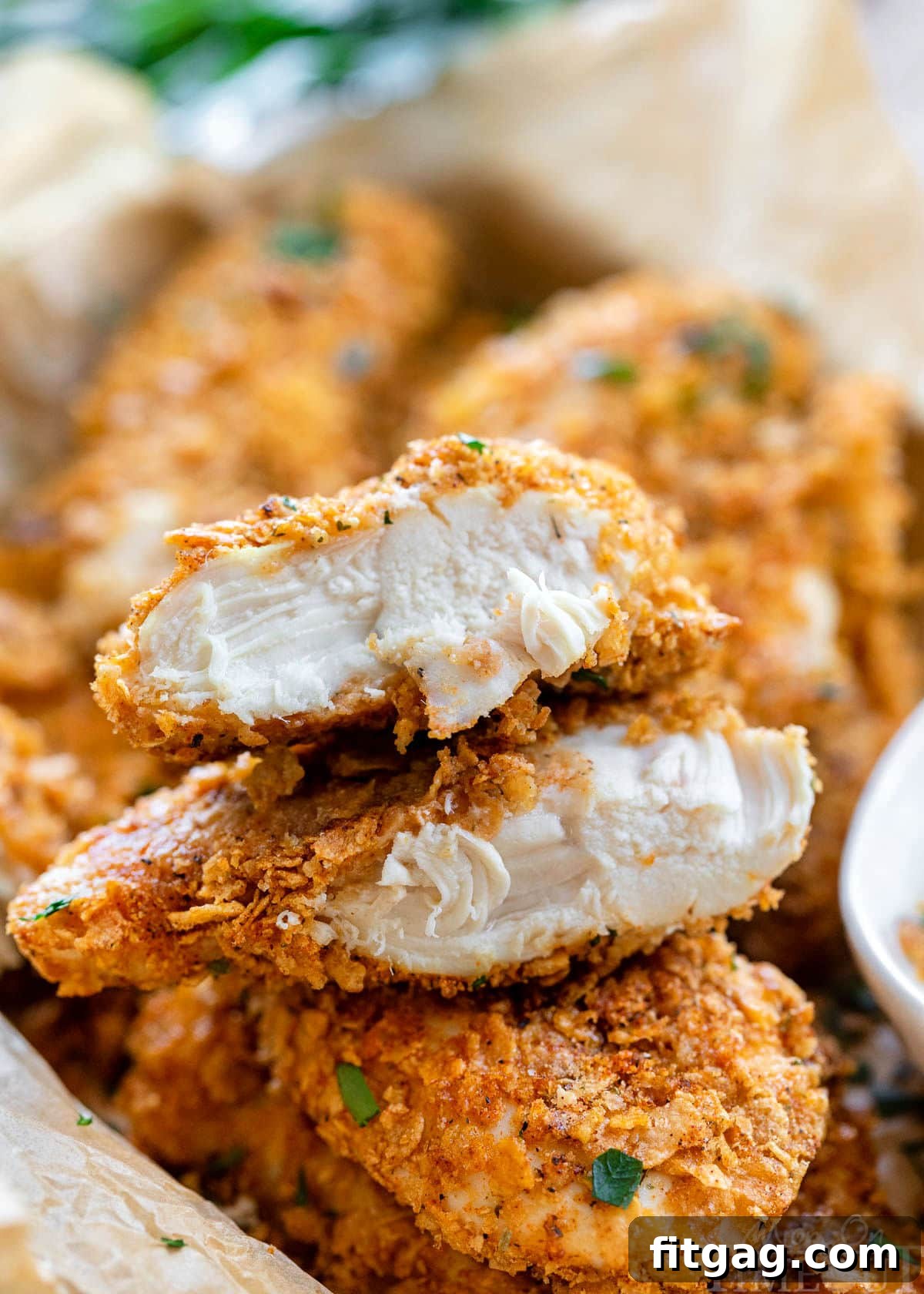 A delectable pile of Cornflake Chicken tenders, perfectly golden and crispy, served with a generous dollop of creamy ranch dipping sauce. One tender is sliced in half and stacked to showcase the moist, tender chicken inside and the crunchy, flavorful coating.