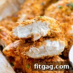 cornflake chicken in a pile with ranch dipping sauce. Top chicken tender is cut in half and stacked on each other showing the moist chicken and flavorful cornflake coating.