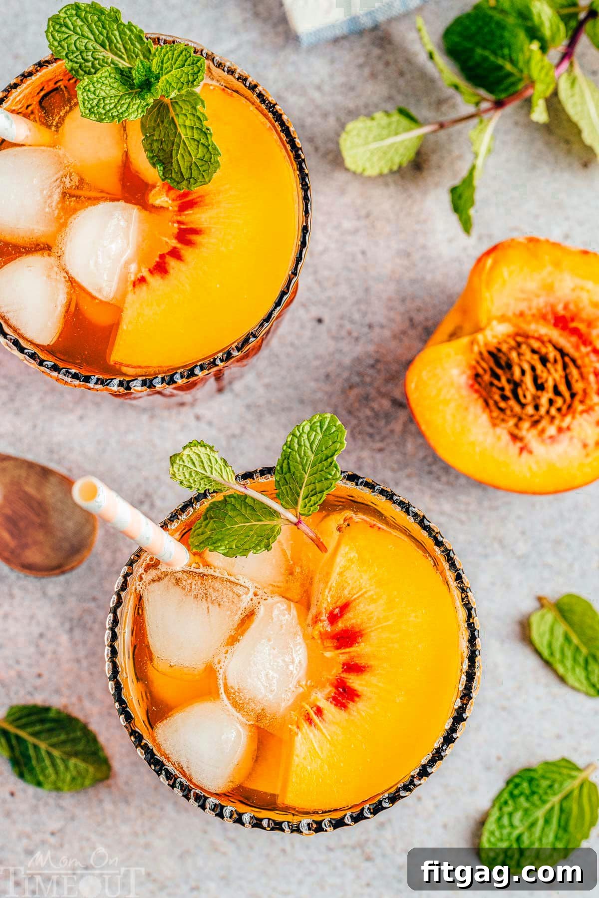 Sun-Kissed Peach Brew 3 top down shot of two glasses of peach iced tea with mint and peach garnishes. both glasses have paper straws in them and half of a peach with a pit in it next to the glasses.