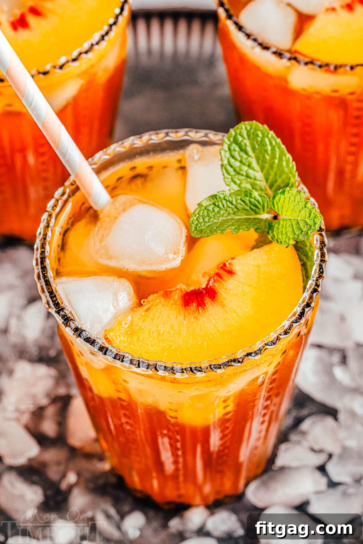Sun-Kissed Peach Brew 8 three tall glasses filled with homemade peach iced tea and topped with fresh peach slices and a sprig of mint. glasses are sitting on a tray covered with ice.