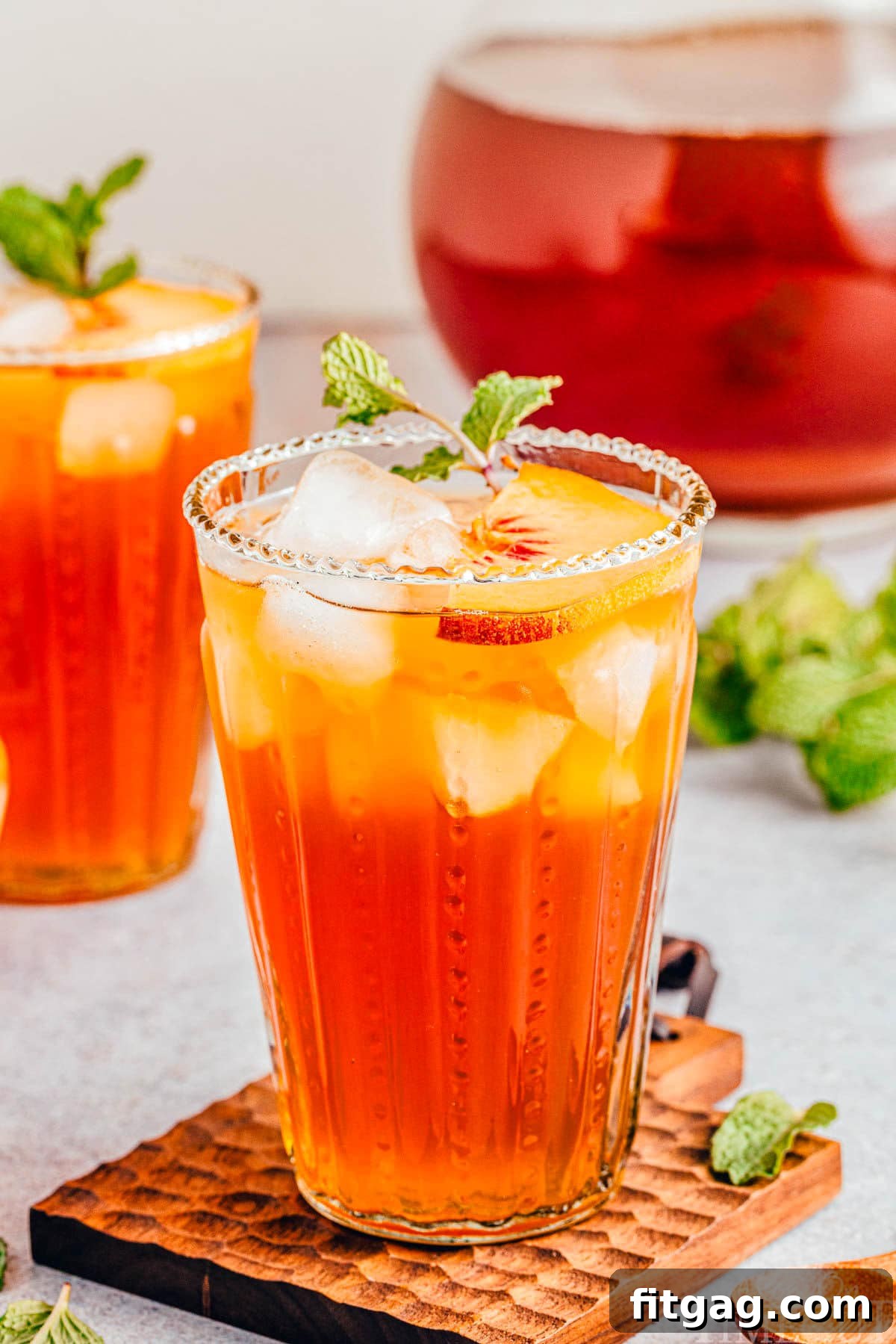 Sun-Kissed Peach Brew 9 tall glass of refreshing peach tea sitting in front of a pitcher of tea and another glass.