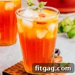 tall glass of refreshing peach tea sitting in front of a pitcher of tea and another glass.