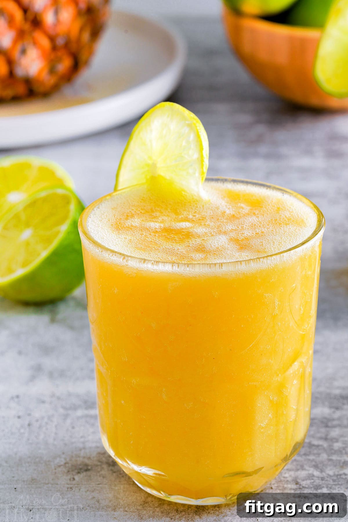 Tropical Bliss Mocktail 3 side view of a pineapple mango mocktail in a glass with a lime wedge garnish on the rim.