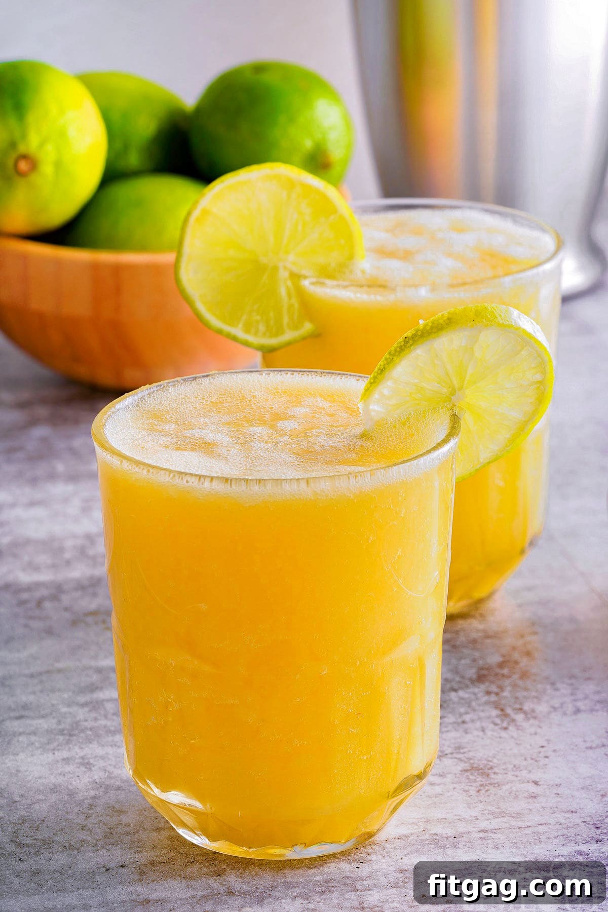 Tropical Bliss Mocktail 5 side view of two glasses of pineapple mango mocktail in a glass with a lime wedge garnish on the rim