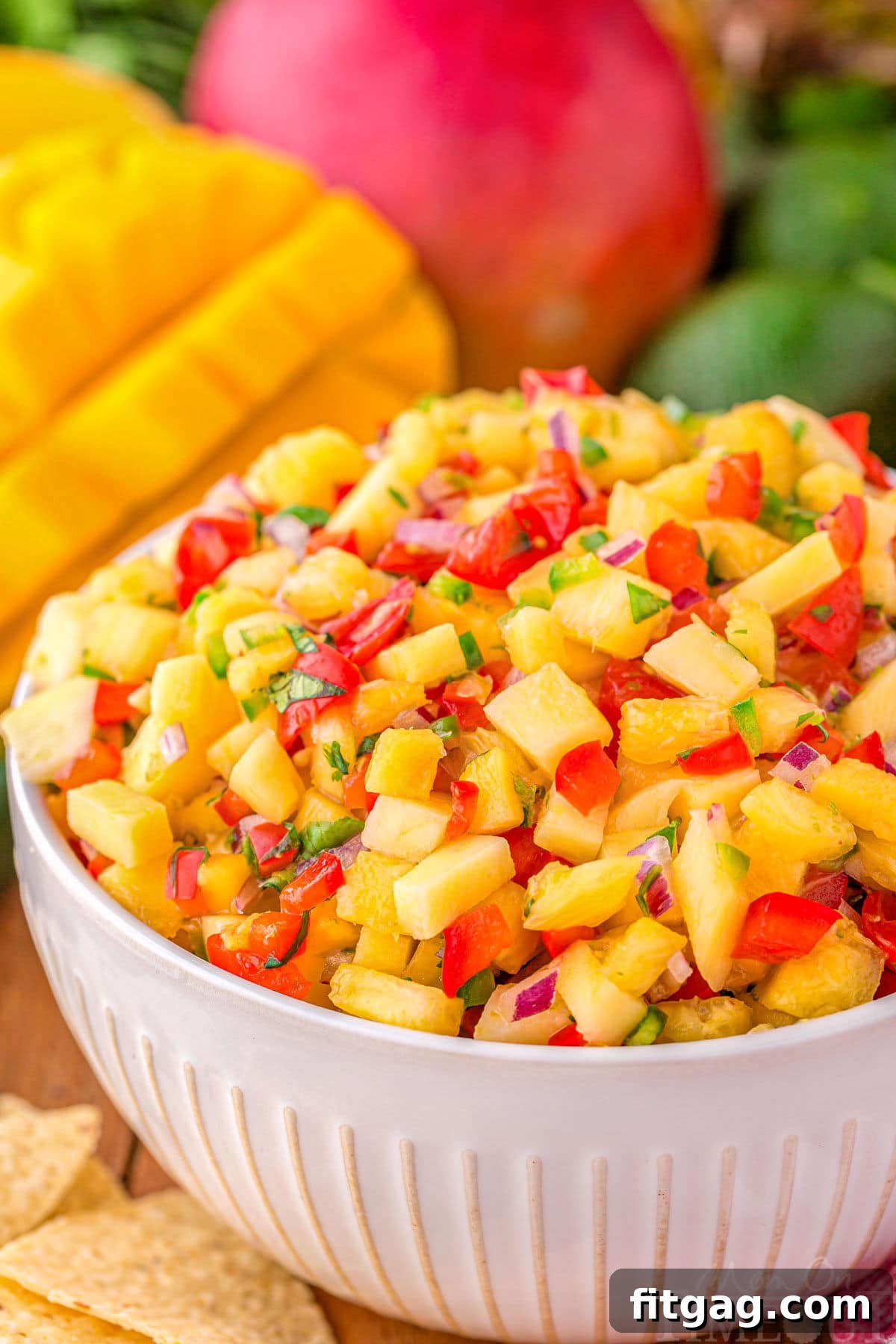 Tropical Pineapple Mango Salsa 2 serving bowl filled withe pineapple mango salsa ready to be enjoyed. Mangoes can be seen in the background.