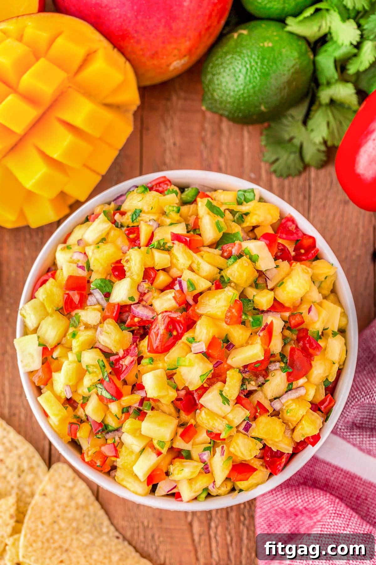 Tropical Pineapple Mango Salsa 6 top down look at pineapple mango salsa in a white bowl surround by chips, mango, limes and cilantro.