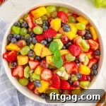Sunshine Fruit Medley 9 A top down view of fruit salad in a white bowl with wood salad tongs sticking out of it.
