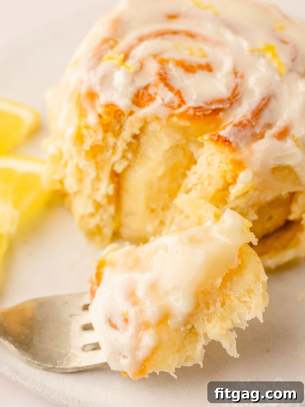 Sunshine Lemon Rolls 3 A single perfectly glazed lemon sweet roll rests on a white plate, with a fork poised beside it, ready to be enjoyed.