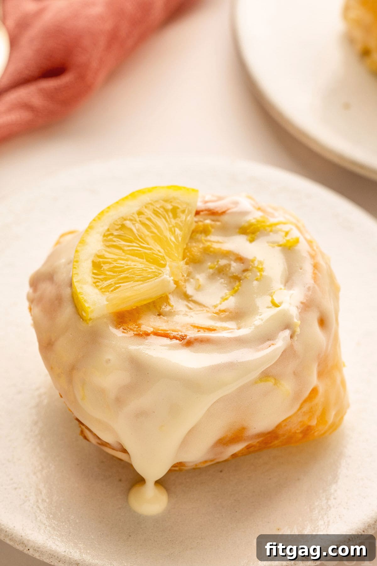 Sunshine Lemon Rolls 4 A close-up side view of a single lemon sweet roll, showing its soft, swirled interior and glistening lemon cream cheese glaze, resting on a crisp white plate.
