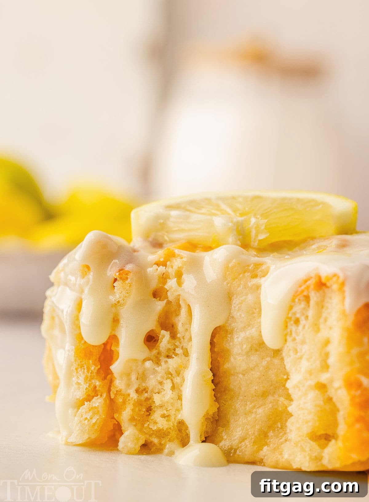 Sunshine Lemon Rolls 7 A close-up side profile of a single lemon sweet roll with a bite taken out, showcasing its fluffy texture and the rich, creamy lemon glaze dripping down its sides.