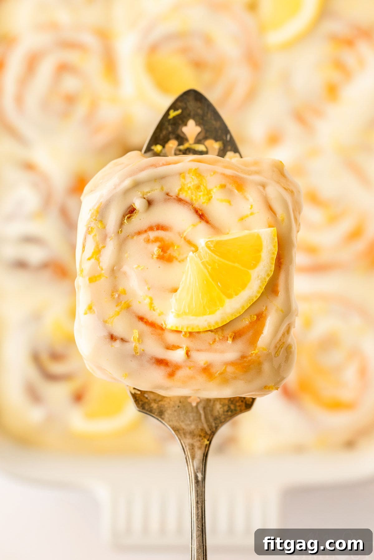 A top-down view of a lemon roll on a spatula, held over the pan of lemon rolls.