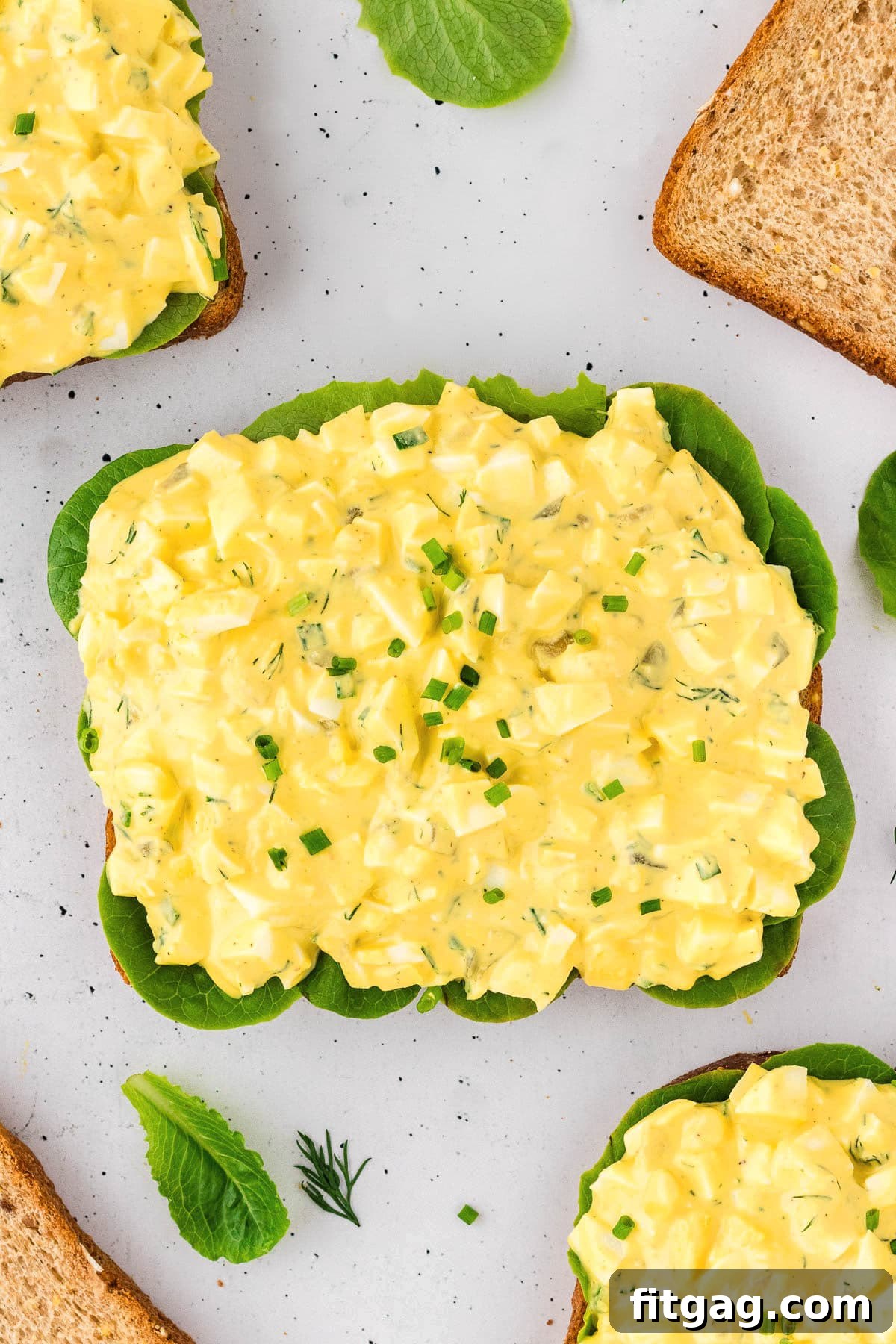 Savory Egg Salad Sensation 6 A top-down view of creamy egg salad generously spread on a piece of rustic bread, garnished with fresh herbs.