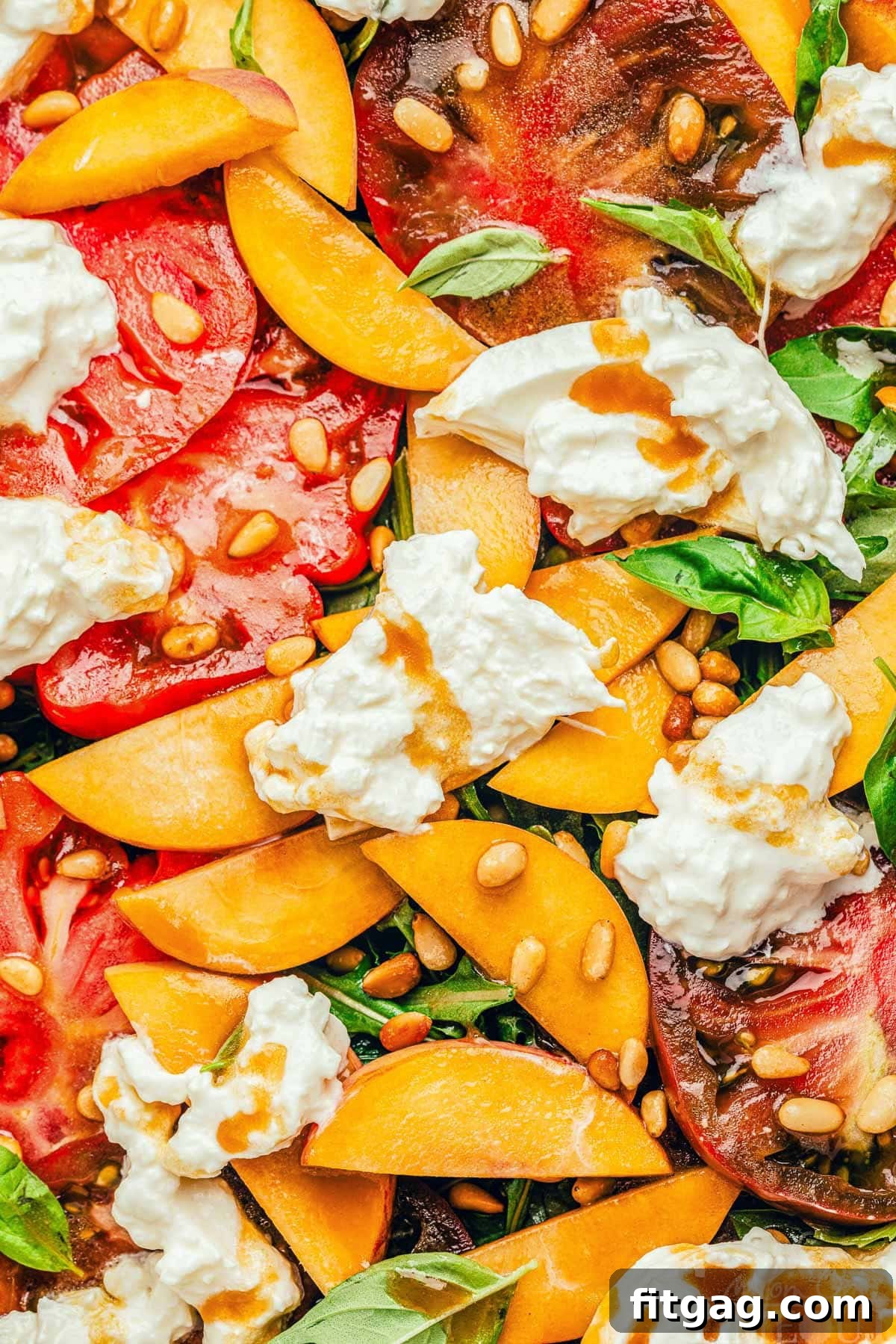 A close-up of a peach and tomato salad on a platter. Slices of peaches and tomatoes rest on a bed of arugula, topped with creamy burrata cheese and drizzled with balsamic dressing.