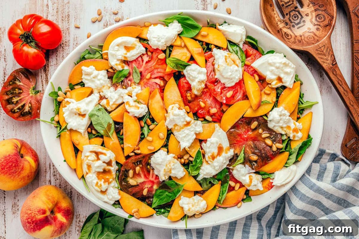 A wide top-down shot of a peach salad on an oval white plate, featuring artfully arranged peaches and tomatoes topping the bed of greens.