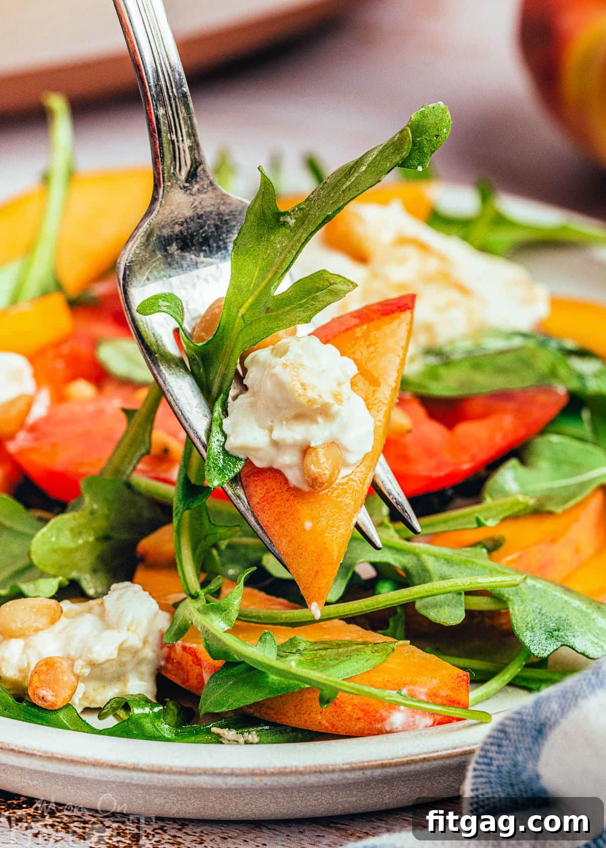A bite of peach burrata salad on a fork, raised above a plate of the same salad, tempting the viewer with its fresh ingredients.