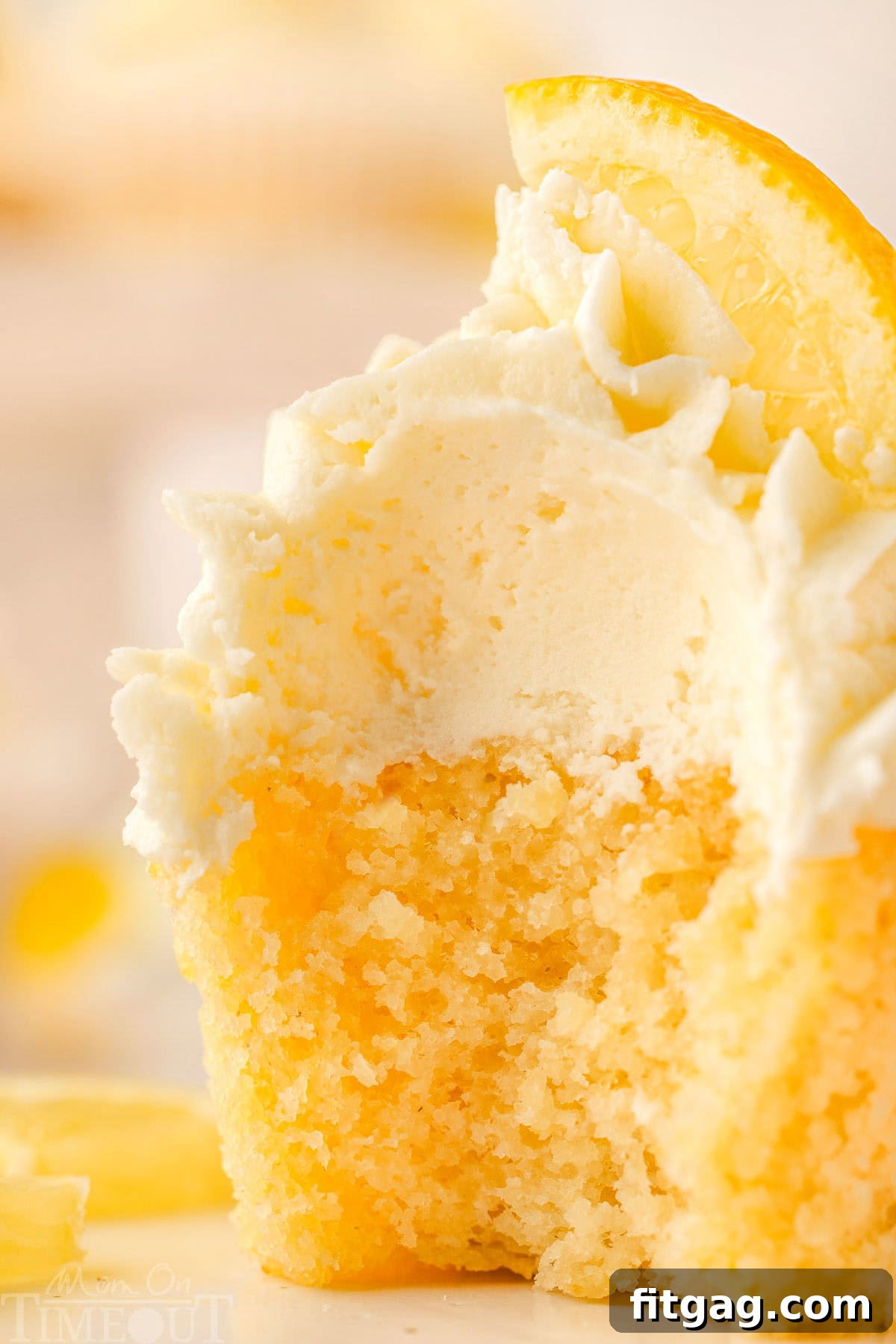 Close-up of a perfectly frosted lemon cupcake with a small bite taken out, revealing its moist yellow interior and hints of lemon zest.
