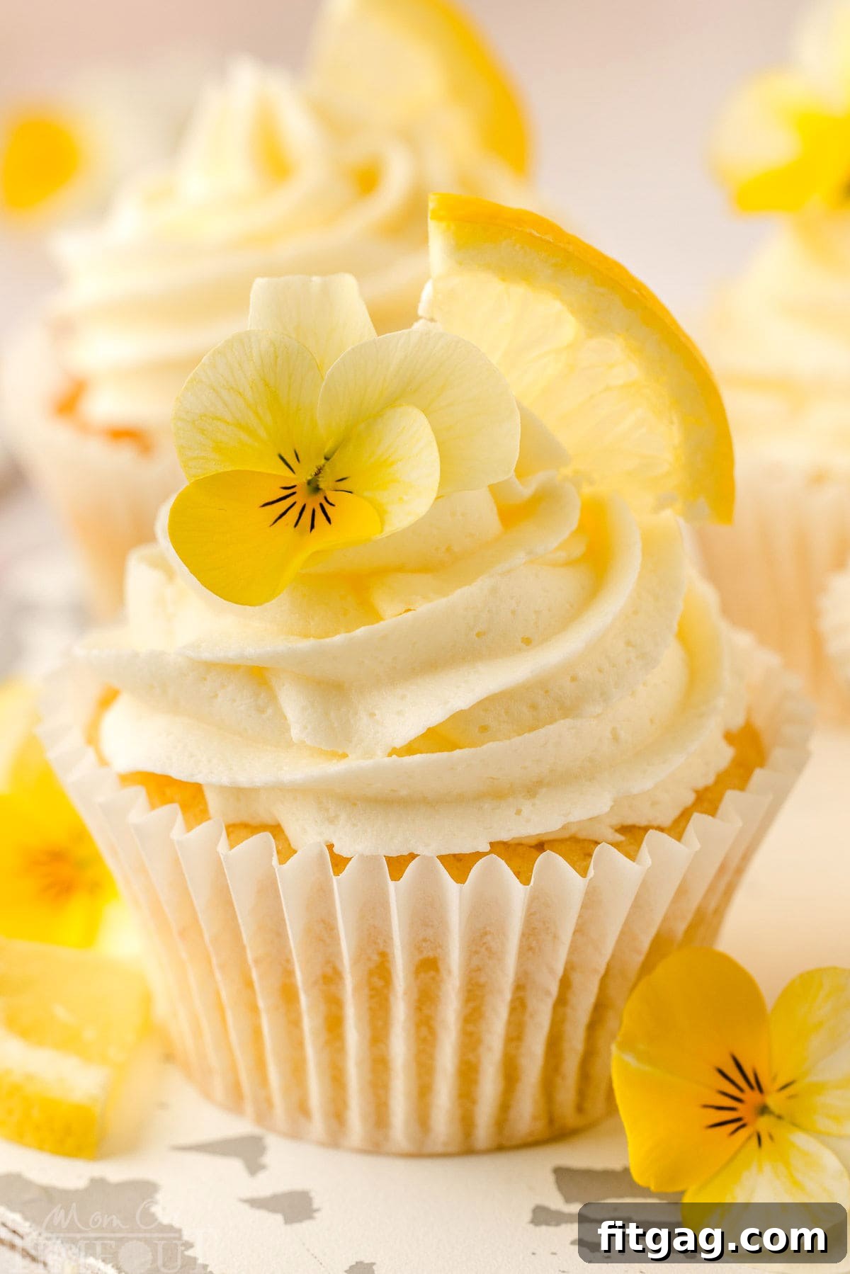 A beautifully frosted lemon cupcake garnished with a fresh lemon wedge and a delicate edible flower, ready to be enjoyed.