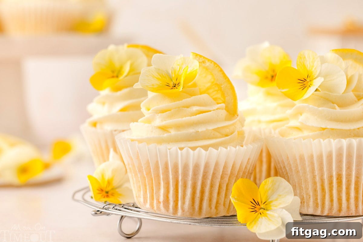 Lemon cupcakes beautifully arranged on a metal cooling rack, frosted with elegant swirls of lemon buttercream and adorned with small yellow pansies.