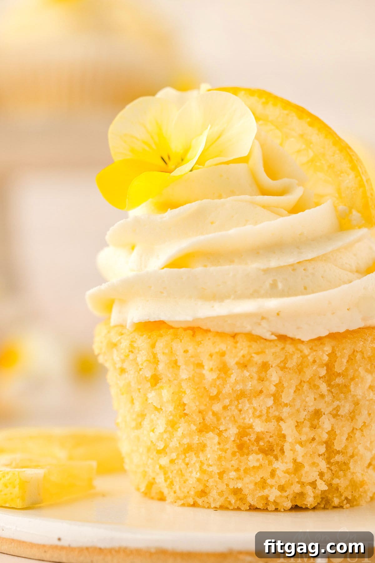 Close-up side view of a single lemon cupcake, artfully frosted and garnished with a lemon wedge and a small edible flower, highlighting its delicate details.