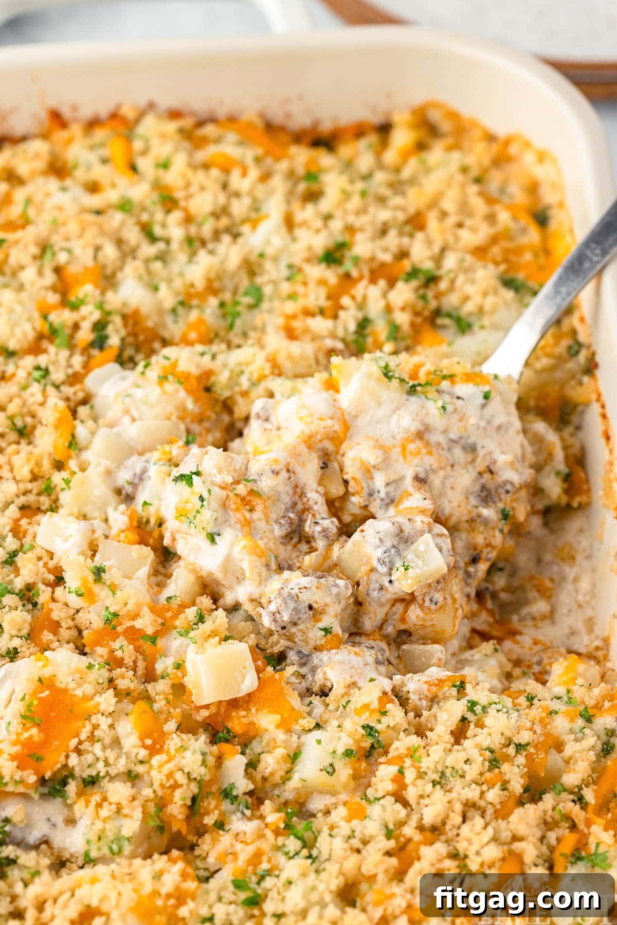 Hearty Beef Bake 7 Ground beef potato casserole in a serving dish with a large serving spoon scooping out a portion.