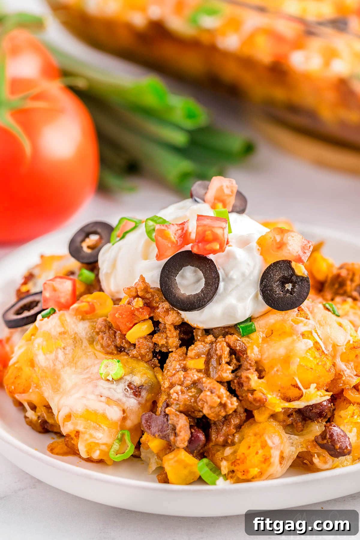 A serving of Mexican tater tot casserole on a white plate topped with sour cream and black olives.