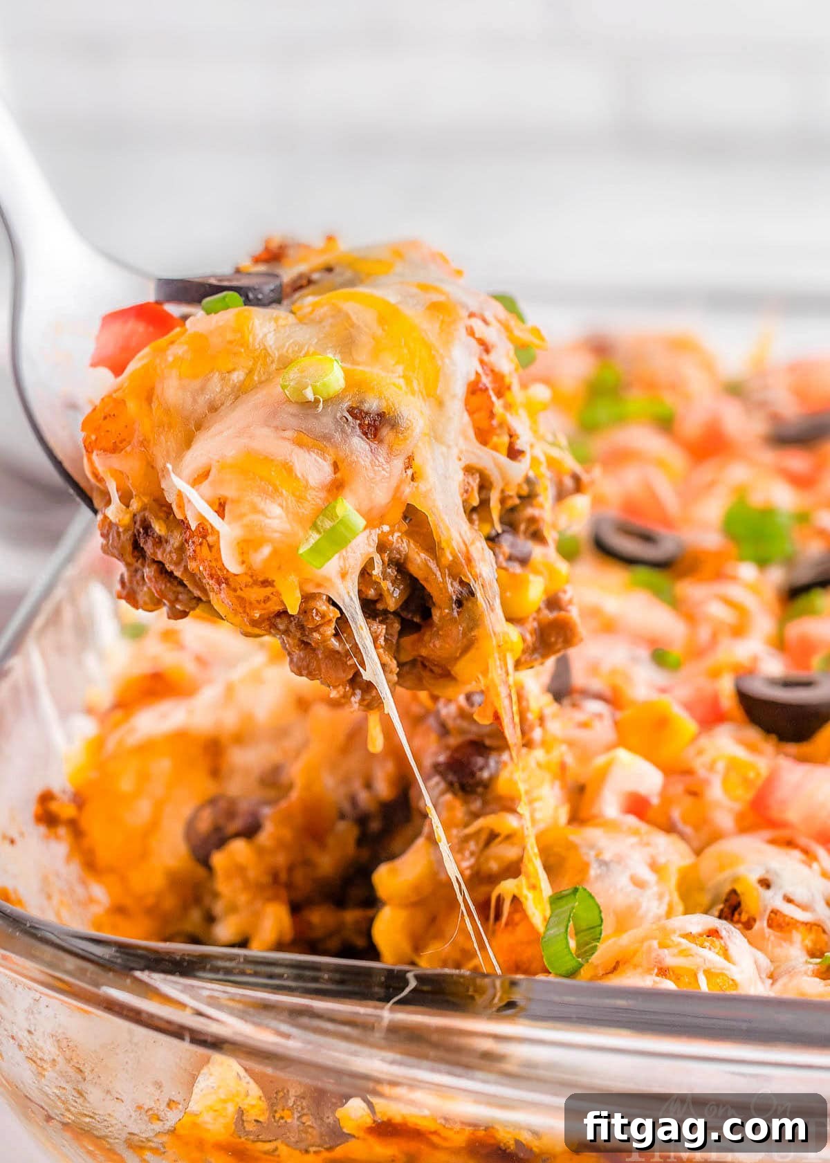 A spatula scooping a piece of mexican tater tot casserole out of a glass pan.