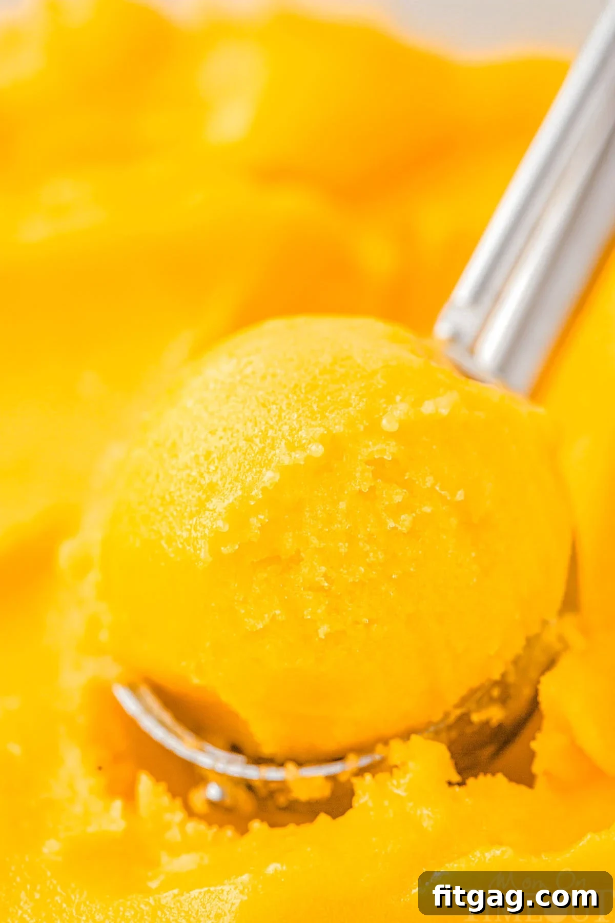 An ice cream scoop delicately scooping smooth, golden mango sorbet from a bowl, highlighting its creamy texture and vibrant color.