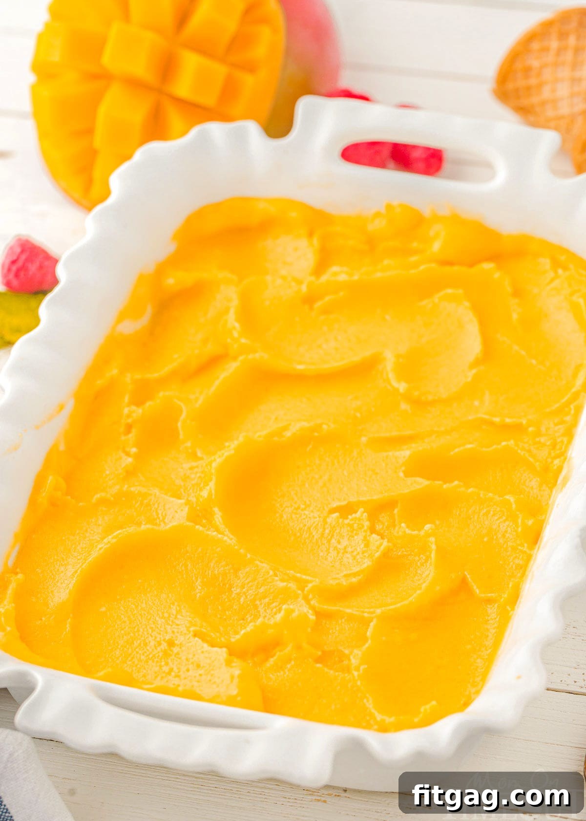 A top-down view of smooth, golden mango sorbet in a white rectangular pan, ready to be scooped and served, highlighting its appealing texture.
