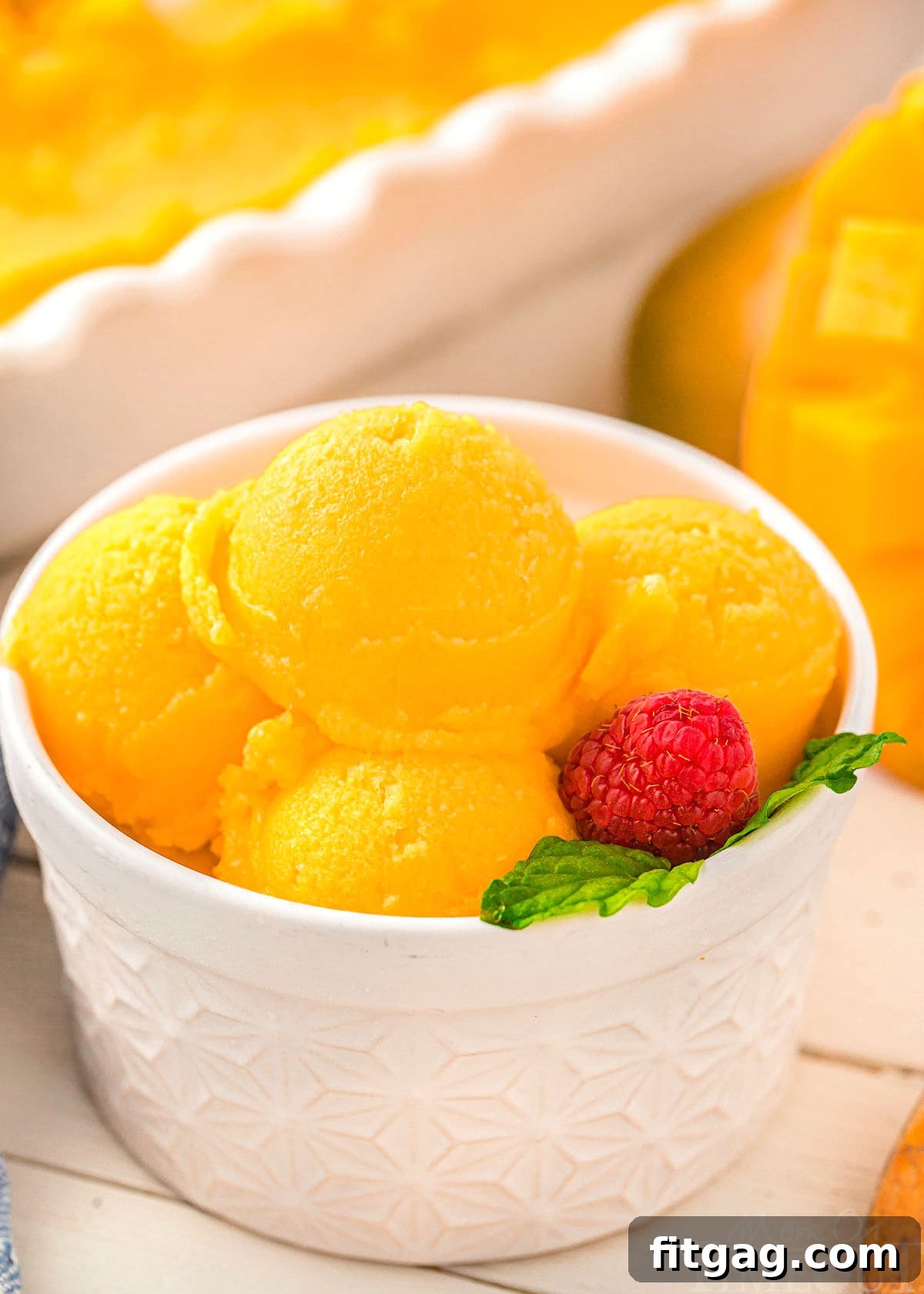 Close-up of scoops of mango sorbet in a white bowl, featuring its smooth texture and rich yellow color, ready to be enjoyed.
