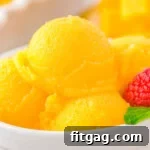 Scoops of mango sorbet in a white bowl topped with fresh mint and raspberries.