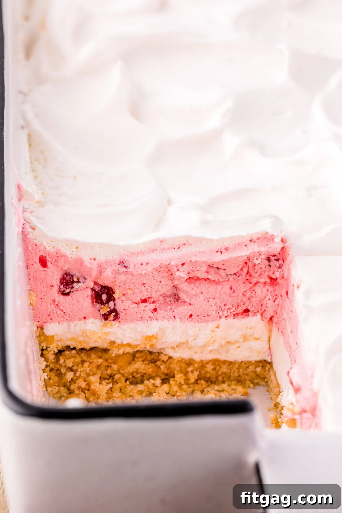 A full baking dish of strawberry lasagna with one slice already removed, showcasing the beautifully defined layers of cookie, cheesecake, and strawberry.
