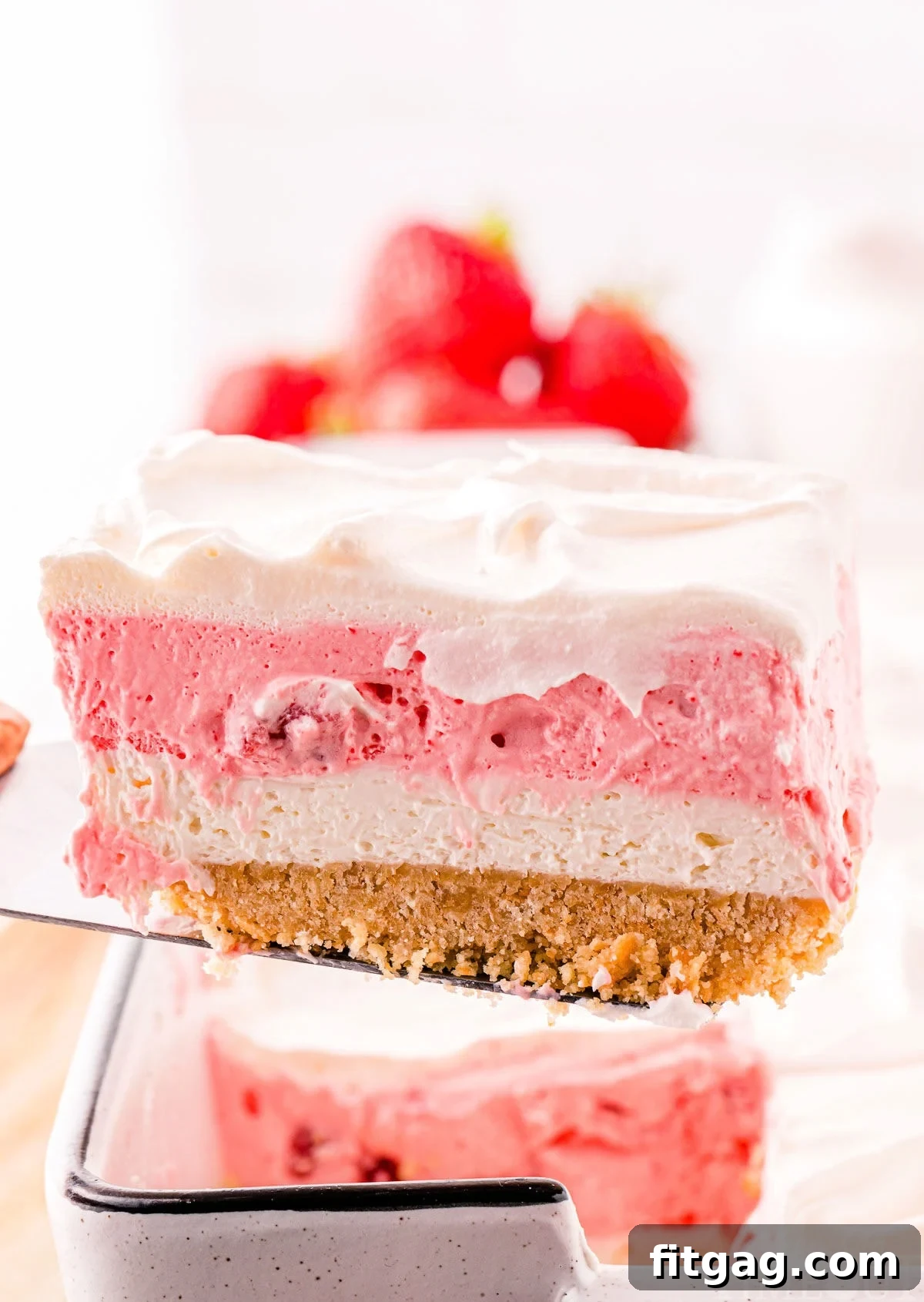 A spatula carefully lifting a single slice of strawberry lasagna from a large baking dish, showing the integrity and neatness of its layers.