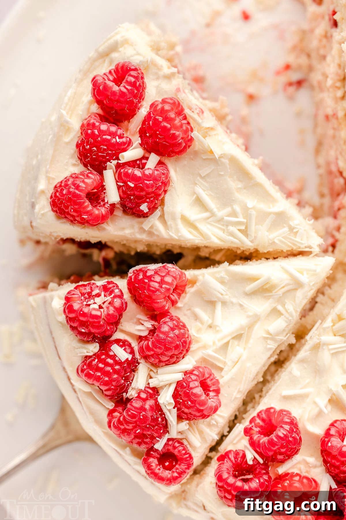Top down look at white chocolate and raspberry cake that has been cut into generous slices. Cake is topped with red raspberries and white chocolate.