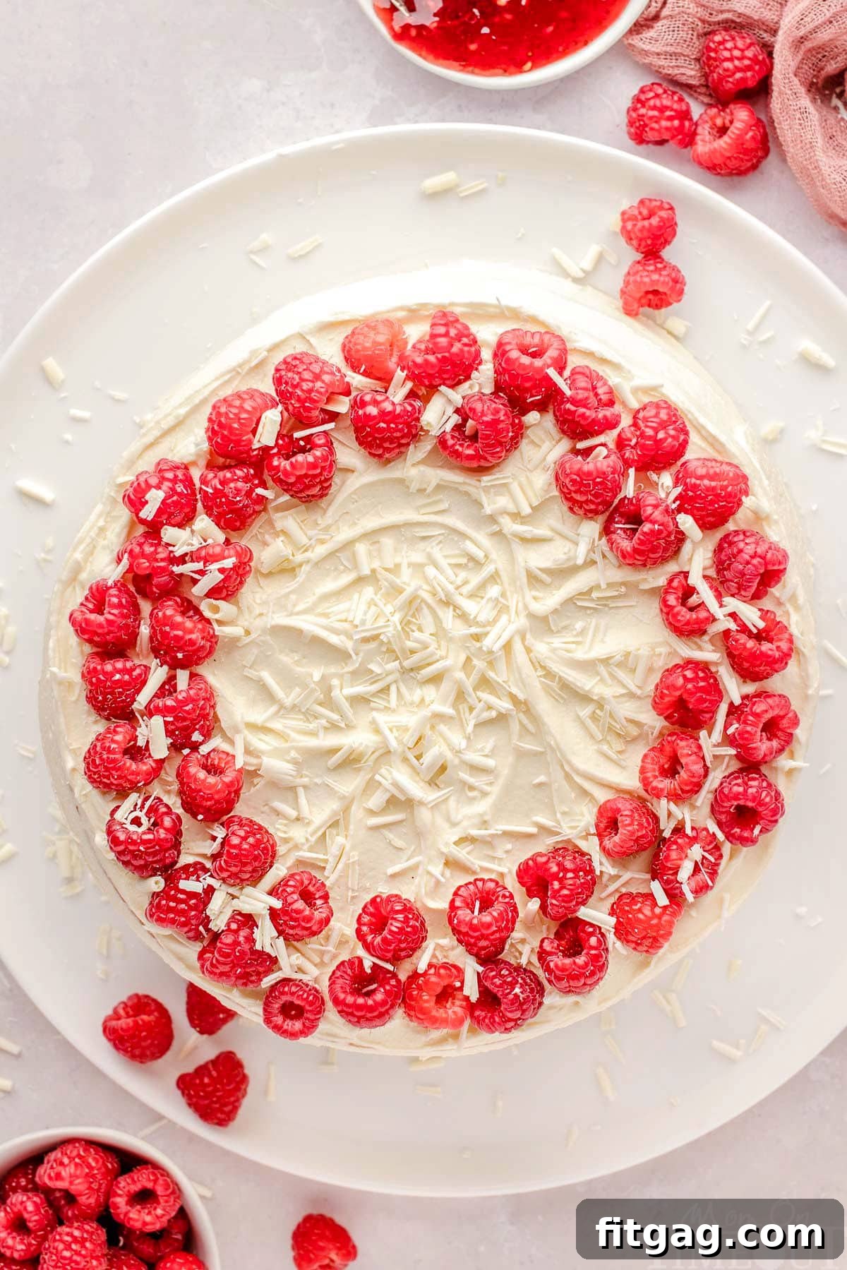 Top down view of whole white chocolate raspberry cake recipe on a large white cake plate. 