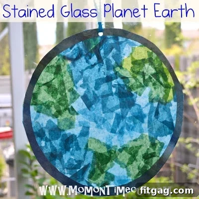 Child's hands tearing green and blue tissue paper into small pieces for a craft project.