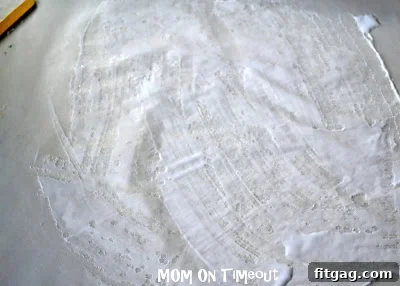 Child carefully placing torn green and blue tissue paper pieces onto the glued wax paper, forming the shape of Earth.