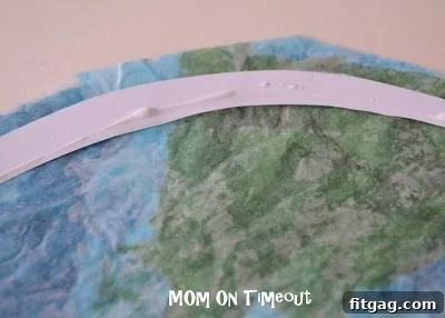 Scissors trimming the excess wax paper around the newly glued paper border of the Stained Glass Earth.