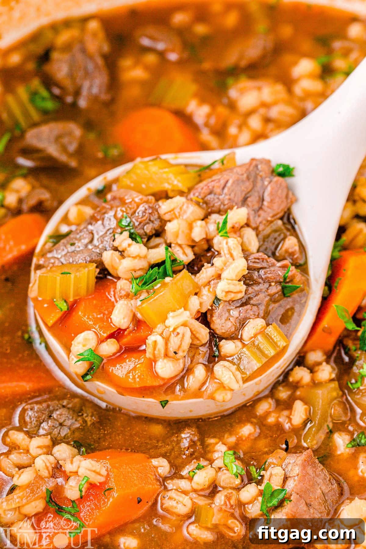 Hearty Beef and Barley Comfort Bowl 2 Beef Barley Soup in a dutch oven with a white ladle scooping out a serving of the soup. The soup has been garnished with fresh parsley.