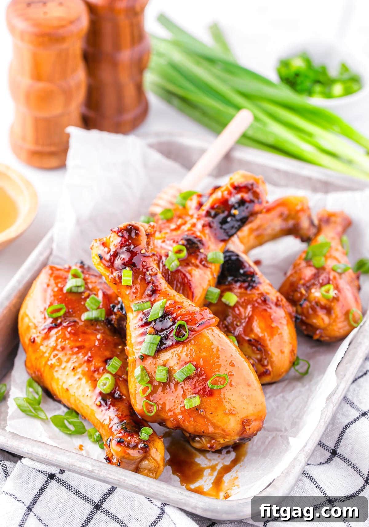 Honey glazed chicken drumsticks on a tray. Green onions can be seen in the background.