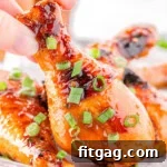 Honey glazed chicken drumstick garnished with green onions being picked up off a small sheet tray with more chicken on it.