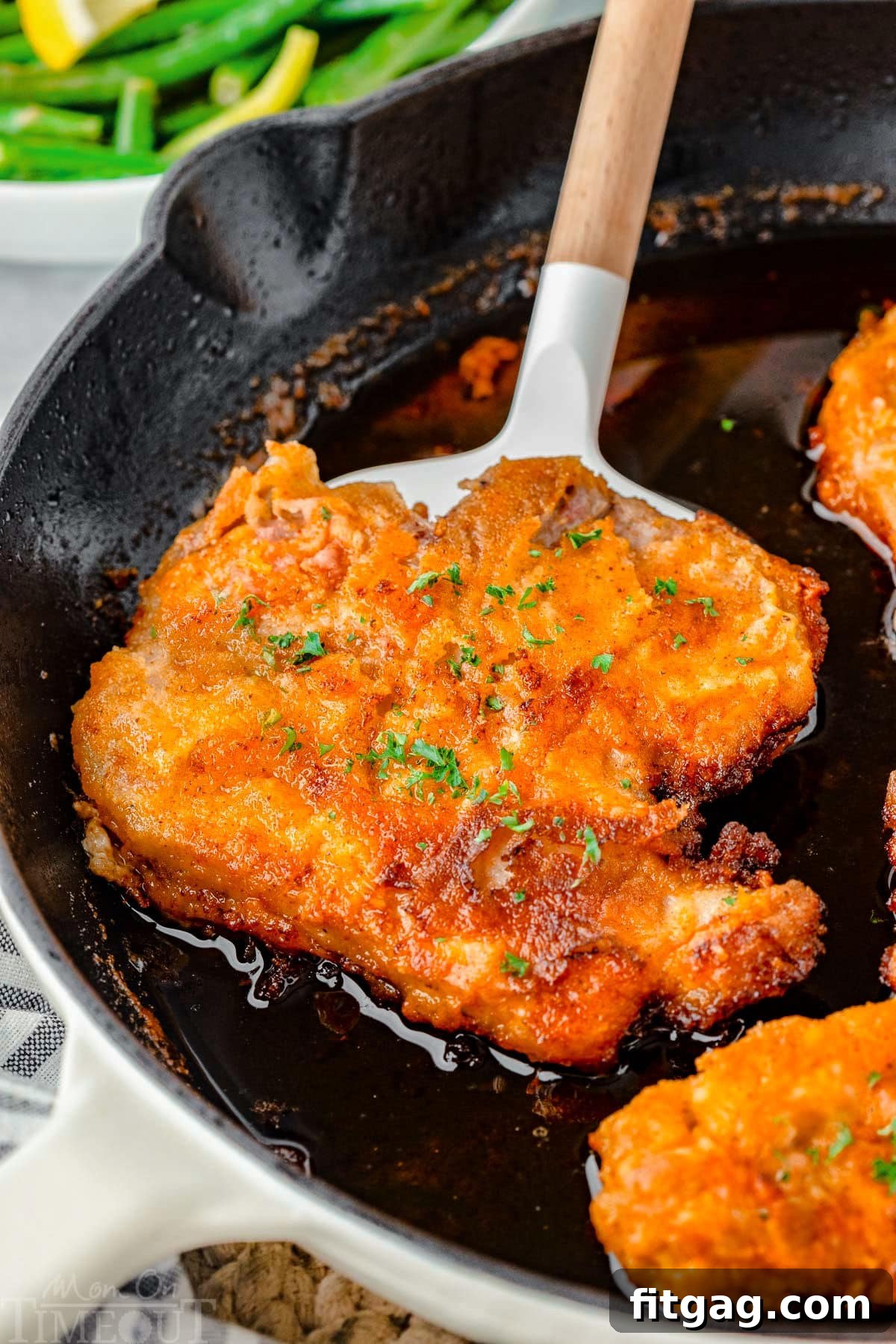 Golden-Crusted Pork Steaks 3 A spatula holding a fried pork chop in a cast iron skilet.