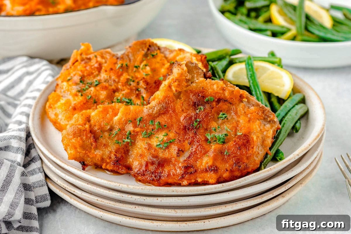Golden-Crusted Pork Steaks 5 Wide shot of two fried pork chops on a stack of plate with green beans.